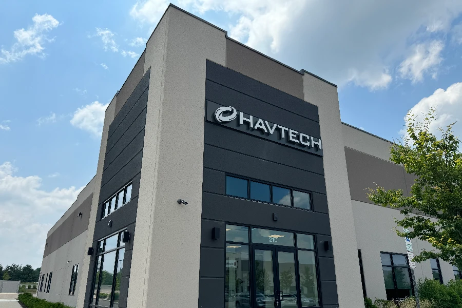 A modern commercial building with the sign "Havtech" on its facade, featuring large windows and a partly cloudy sky in the background.