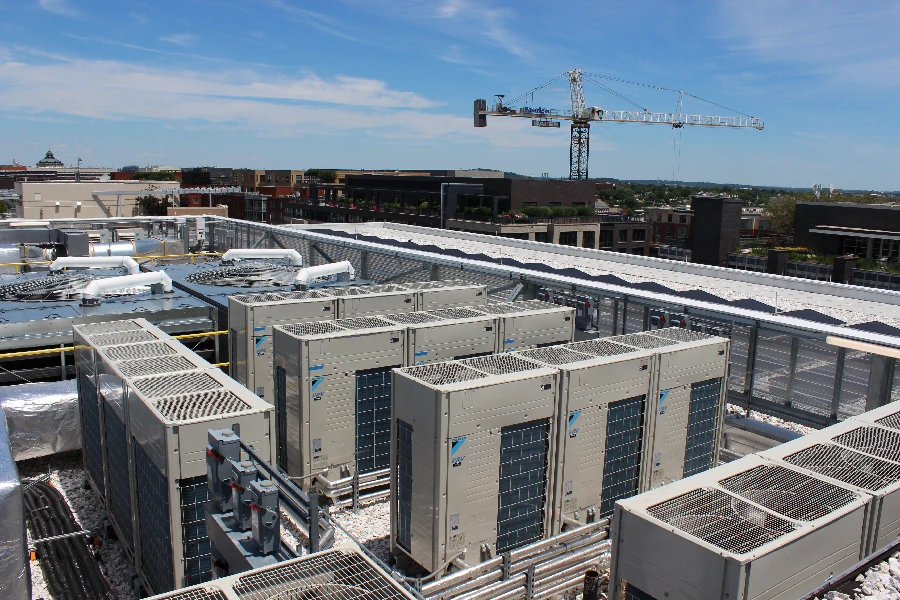 Rooftop view of multiple industrial HVAC units with buildings and a construction crane visible in the background under a blue sky.