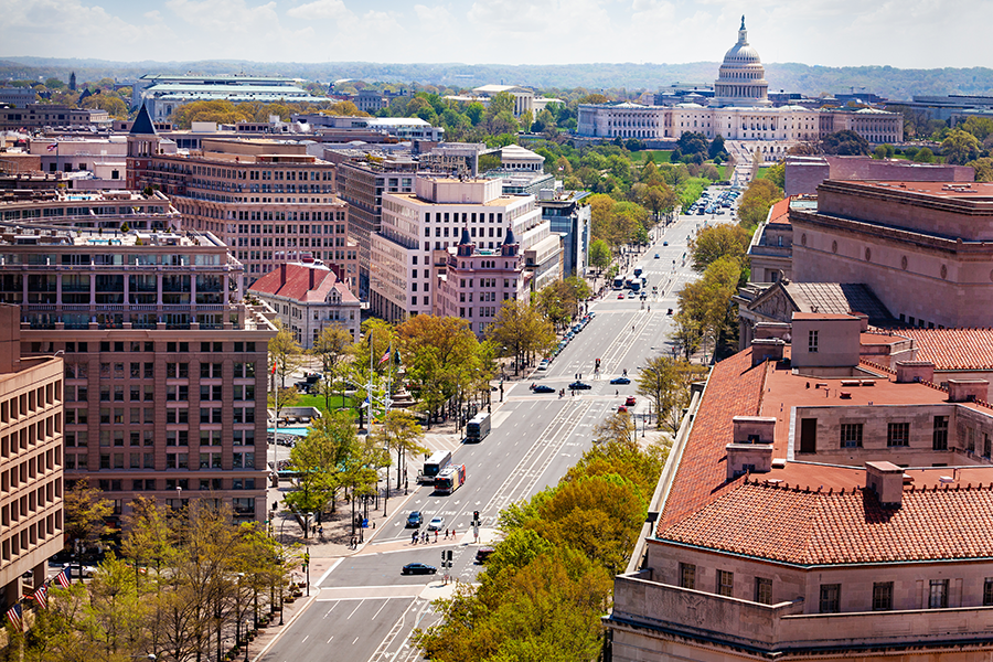A wide view of Pennsylvania Avenue in Washington, D.C. with the U.S. Capitol building visible in the background and several city buildings lining the street.