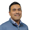 Mauricio Salinas, with short dark hair wearing a blue quarter-zip sweater over a plaid collared shirt, photographed against a white background.