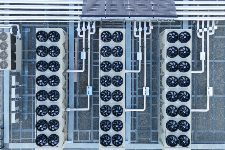 Aerial view of three large data center heat rejection units with multiple fans, connected by white pipes on a metal grate roof.